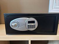 Closed black steel security safe showing electronic keypad lock and a turning knob on front.