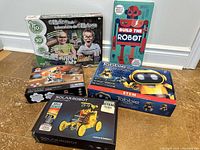 Five STEM and robot-building toy sets arranged on the floor: Science4you Coding Lab, Build the Robot kit, Tobbie the Robot, Solar Robot, and another small robot set.