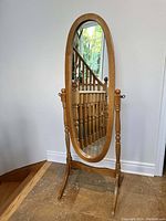 Full view of swinging full-body oval floor mirror standing on floor with wooden banister in background.