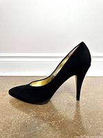 Side view of a single black satin high heel shoe showing the pointed toe, smooth matte finish, and slim heel.