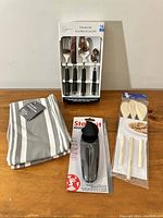 Photo showing all items in the lot: boxed 16-piece flatware set, two striped kitchen towels, black-handled can opener, and three wooden spoons packed together