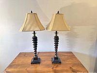 Two full lamps with spiral wooden bases and cream satin shades on wooden surface