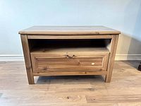 Front view of the wooden TV stand showing the drawer with handle and open shelf above it.