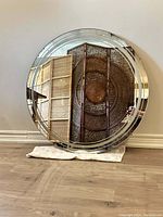Full view of the large vintage round wall mirror leaning against a wall on a wooden floor.
