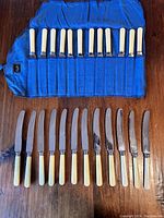 Photo showing 12 Maleham & Yeoman dinner knives with cream-colored handles laid out on blue cloth roll, blades facing downward