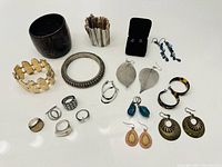 Full view of assorted bracelets, rings, and various earrings spread on surface.