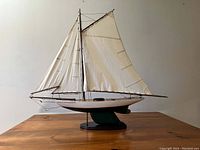 Full side profile of wooden tri-sail schooner model with three white canvas sails on wooden masts, mounted on black stand.
