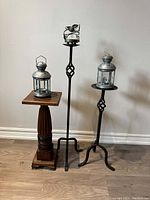 Full view of two wrought iron candle stands with metal candle lanterns on top and the wooden fern stand with a lantern placed on it