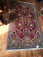 Full view of the darker burgundy area rug with floral patterns and fringed edge on wooden floor