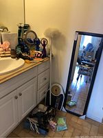 Full view of bathroom counter and floor showing various items included in lot such as mirror, scale, hair dryer, curling irons and other bathroom accessories