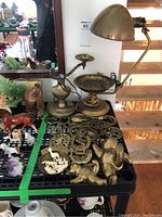 Wide shot of brass collection including desk lamp, ashtray with compartments, brass figurines, horseshoe-shaped items, and small brass decorative pieces.