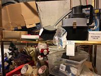 Wet and dry auto vacuum cleaner with handle, black and grey in color, along with a broom head, rolls of tape, and miscellaneous painting supplies on a shelf.