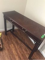 Full view of a dark wood console table with a rectangular top and four legs, showing surface wear.
