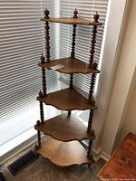 Full view of the wooden corner shelf showing all five tiers, turned vertical supports, and decorative finials at the top.