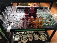 Top view of assorted glassware including clear etched, red ruby cobalt, amber gold accented glasses, and green stem glasses
