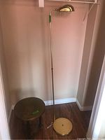 Full view of adjustable brass floor lamp standing beside small round side table with greenish top.