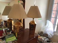 Pair of gold-tone metal lamps with hexagonal bases and beige pleated shades placed on wooden table in front of a mirror.