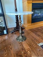 Side view of the marble top side table showing the round white marble top with scalloped edges and the antique bronze cast metal ornate base.