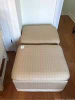 Two beige upholstered ottomans stacked, showing size and upholstery pattern.