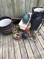 View of assorted garden planters of various shapes, sizes and materials, plus a green plastic watering can and some garden decorations on wooden deck.