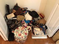 Closet floor pile showing assorted purses, scarves, belts, hats, and two hat boxes including a floral fabric covered box and assorted fabric and straw hats.