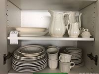 Upper shelf with large serving pitchers, creamers, covered sugar bowl and serving plates.