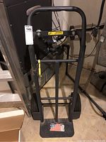 Front view of the black metal hand truck with large wheels and a flat loading plate with an American flag sticker.