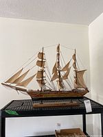 Front and side view of the wooden model ship on a black rack showing full rigging and sails.