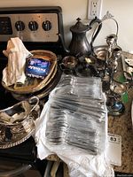 Various silver plate cutlery and serving items arranged on a kitchen counter and stove.