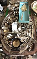 Silver plated large trays filled with assorted spoons, forks, small creamers, and other serving utensils, showing tarnish and wear.