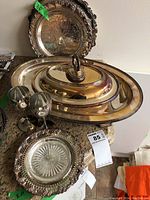 Photo of multiple silver-plated trays, a covered serving dish, two goblet glasses, and a tray with glass plate insert