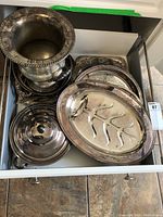 Overview of multiple silver plated serving dishes stacked inside a drawer including platters, a covered dish, and shallow bowls.