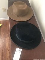 Two Stetson hats placed on a dark surface, one tan and one black, showing overall condition and style.