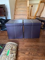 Two brown vinyl storage seats with padded tops placed side-by-side on wooden floor near stairs