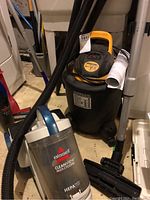 Shop-Vac wet/dry vacuum and Bissell Cleanview Multi-Cyclonic vacuum placed side by side on floor.