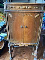Front view of wooden Victrola phonograph cabinet with ornate carved doors and turned legs, showing overall condition and design details including knobs and molding.