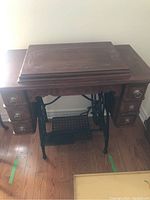 Photo of the wooden cabinet with drawers and treadle pedal base, showing the sewing machine covered by a wooden lid.