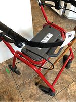 Front and seat view of red Dolomite Legacy 600 walker showing grey molded seat and hand brakes with black grips, on tiled floor