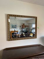 Full view of large wall mirror with sculpted wood frame mounted on a wall above furniture, showing overall size and setting.