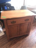 Front view of wooden washstand with drawer and double doors on wood floor in room.