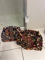 Two Vera Bradley fabric purses with colorful floral designs placed on tiled floor.