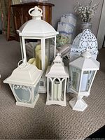 Group of five white decorative lanterns including a large Duraflame lantern space heater and four other white lanterns with faux candles placed on carpet.