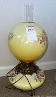 Full view of the round yellow glass lamp with floral painting and ornate brass base, showing the lamp's height and condition.