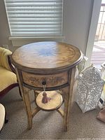 Side view of an oval wooden table with a painted top, drawer, tassel pull, and decorative legs beside a window.