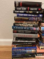 Stack of assorted novels showing titles by Herman Wouk, Stuart Woods, Amy Tan, Scott Turow, Ridley Pearson, Michael D'Antonio Patterson, and James Patterson.
