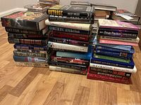 Photo showing multiple stacks of hardcover and paperback novels with varied titles and authors, including works by George R. R. Martin, Vincent Bugliosi, and others.
