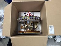 Top-down view of the Christmas carousel displayed inside a cardboard box showing the entire carousel with the striped red and white canopy.
