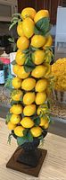 Artificial lemon tree with several bright yellow faux lemons and green leaves on a black pedestal base with a wooden square base.