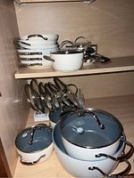 Top cabinet shelf showing stacked frying pans and two saucepans/stockpot with lids