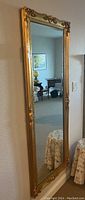 Full-length view of gold-framed mirror hanging on wall, showing overall dimensions and reflective surface
